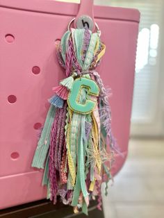 a pink purse with the letter g hanging from it's front loop and tassels