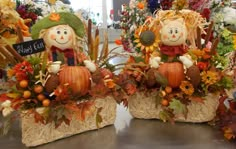 two scarecrows sitting on hay with pumpkins and leaves