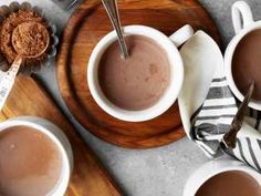 three cups of hot chocolate on a wooden tray with spoons and napkins next to it