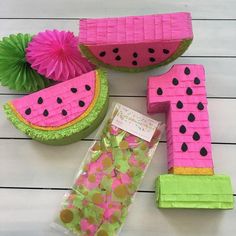 some pink and green paper decorations on a white wooden table with watermelon slices