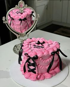 a heart shaped cake with pink frosting and black ribbon on top, sitting in front of a mirror