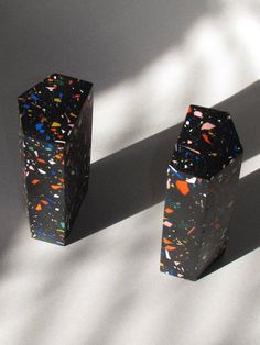 two black vases sitting next to each other on a white surface with colorful sprinkles