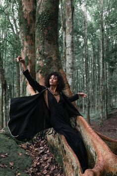 a woman is sitting on a tree trunk in the woods with her arms spread out