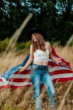 a beautiful young woman holding an american flag while standing in the middle of tall grass