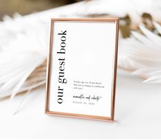 a white and gold frame sitting on top of a table next to some feathers in front of it