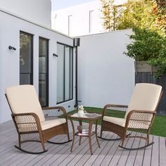 two chairs and a table sitting on a wooden deck next to a white wall with windows