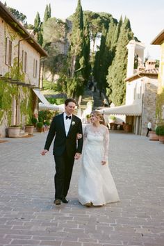 a bride and groom walking down a cobblestone road in front of some buildings