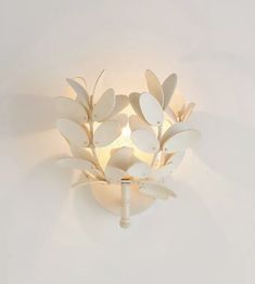 a white wall mounted light with leaves on it's side and a candle in the middle