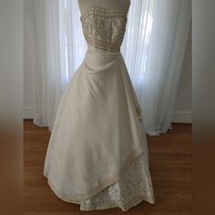 a wedding dress on display in front of a window with white curtains and wooden flooring