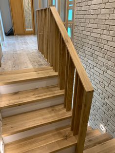 there is a wooden stair case in the house with white brick walls and wood handrails