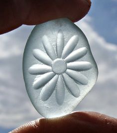 a hand holding a plastic object in front of a blue sky with clouds behind it