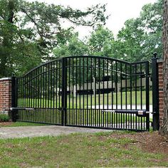 an iron gate in front of a brick wall and tree with grass on the ground