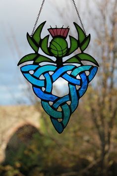 a stained glass sun catcher hanging from a chain with leaves and flowers in the center