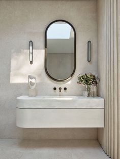 a white sink sitting under a round mirror next to a wall mounted faucet