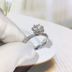 a close up of a person's hand holding a ring with a diamond on it