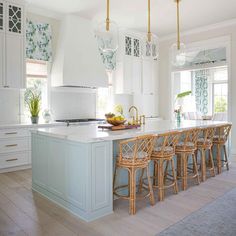 a kitchen with white cabinets and light blue island in the center is surrounded by wicker bar stools