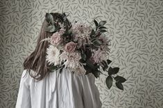 a woman standing in front of a wall with flowers on her shoulders and long hair