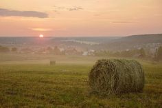 a field with hay bales in the foreground at sunset