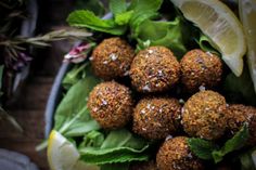 a bowl filled with meatballs covered in seasoning next to lemon wedges