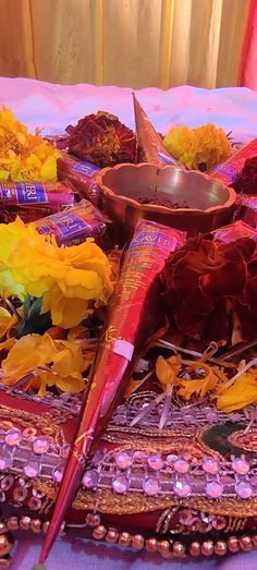 a table topped with lots of flowers next to a metal bowl on top of a purple cloth