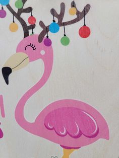 a pink flamingo painted on the side of a white wall with christmas ornaments hanging from it's branches