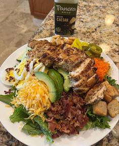 a white plate topped with meat and salad next to a bottle of beer on a counter