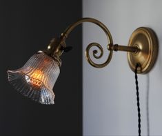 an old fashioned wall light with a glass shade on it's arm and the bulb turned off