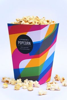 a colorful popcorn box filled with lots of popcorn kernels on top of it's side