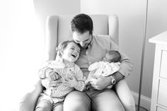 a man sitting in a chair holding a baby and smiling at the camera while he holds it up to his chest