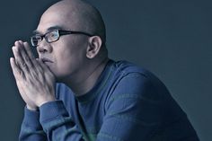 a bald man with glasses is holding his hands to his face and looking off into the distance