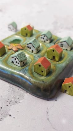 small ceramic houses sitting on top of a green tile tray with holes in the middle