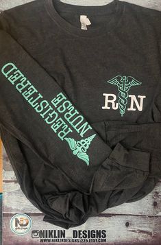 How perfect is this long sleeve lightweight T-shirt that is also soft feel, a great addition to anyone's closet for the Hard working nurse. Great for the in between weather is this shirt. It features the caduceus in teal and Rn in white on the Front left chest of the shirt and down the sleeve it has registered nurse with the caduceus in turquoise writing. No way can anyone go wrong with this top. Tear-away label Ribbed cuffs Sideseamed Retail fit Triblends - 3.8 oz., 50% poly, 25% combed ringspu Gray Long Sleeve Pre-shrunk T-shirt, Relaxed Fit Long Sleeve Nursing Top, Casual Long Sleeve Nursing Tops, Casual Long Sleeve Nursing T-shirt, Long Sleeve Cotton Nursing Tops, Nurse Clothing, Nurse Decals, The In Between, Heat Press Machine