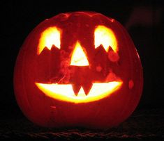 a jack o lantern pumpkin lit up in the dark with its mouth open and glowing