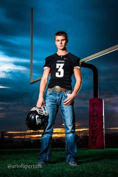 a young man wearing a football uniform and holding a helmet standing in front of a goal post