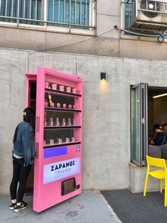 a pink vending machine sitting in front of a building next to a yellow chair