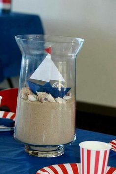 a table topped with plates and cups filled with sand next to a sailboat in a glass vase