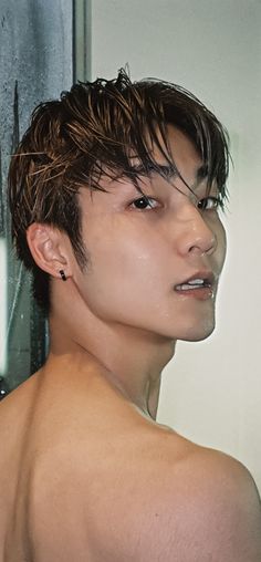 a man with wet hair standing in front of a shower head and looking off into the distance