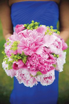 a woman in a blue dress holding a bouquet of pink and white peonies