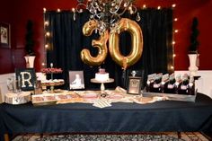 a table topped with lots of cake and balloons in front of a black curtained wall