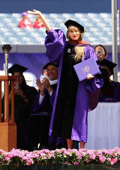 a woman in purple graduation gown waving to the crowd