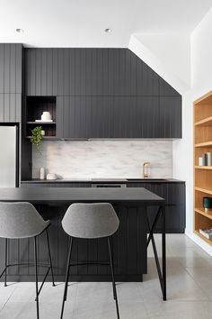 a kitchen with black cabinets and two chairs in front of the counter top, next to an open shelving unit