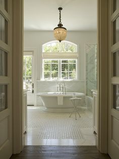 an open door leading to a bathroom with a claw foot tub in the middle and a chandelier hanging from the ceiling