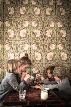 three children sitting at a table eating food and drinking milk from glasses in front of them