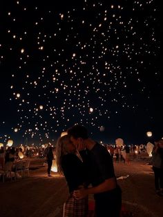 a man and woman kissing under the night sky full of balloons that are floating in the air