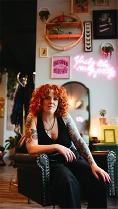 a woman with red hair sitting in a chair next to a mirror and neon sign