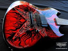 a red and black guitar with an intricate design on it's body, sitting on a black background