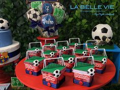 a table topped with lots of cakes and soccer themed items on top of a red table