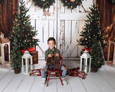 a young boy sitting on a chair in front of christmas decorations and trees with lights