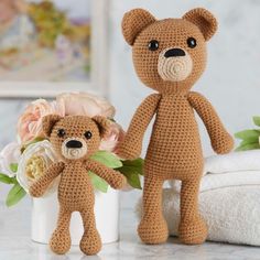 two crocheted teddy bears sitting next to each other on a table with flowers