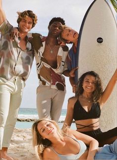 four people are posing with a surfboard on the beach